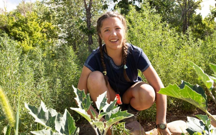 a student who is working in a garden smiles at the camera